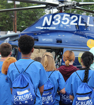 Students at a Scrubs camp event next to an EMS helicopter.