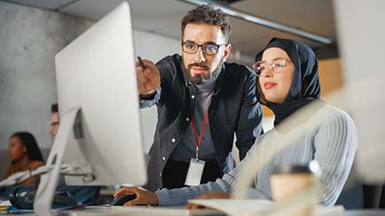 Student eagerly reviewing online course materials with instructor pointing at computer monitor