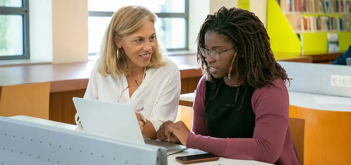 Instructor assisting student on laptop in classroom